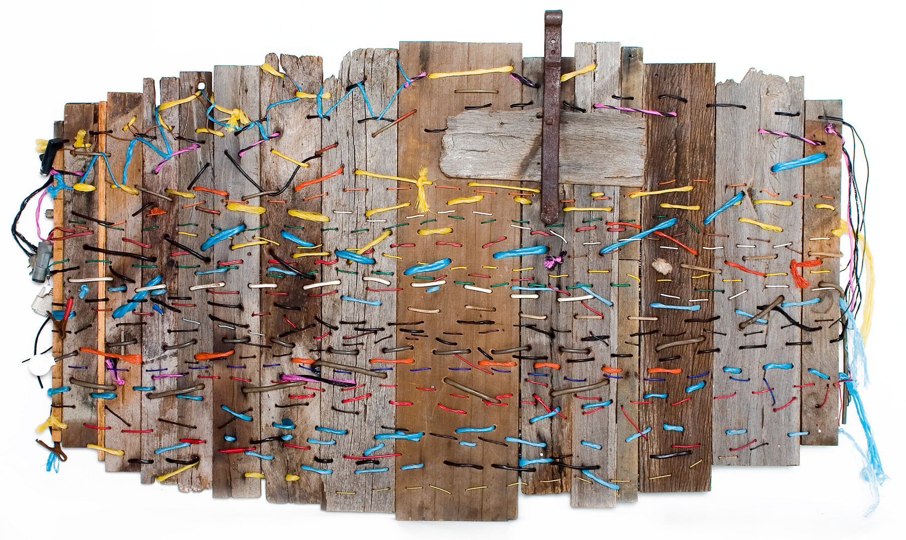 Dozens of narrow weathered boards of different heights set side by side, woven through with strands of yellow, blue, red and white thread.